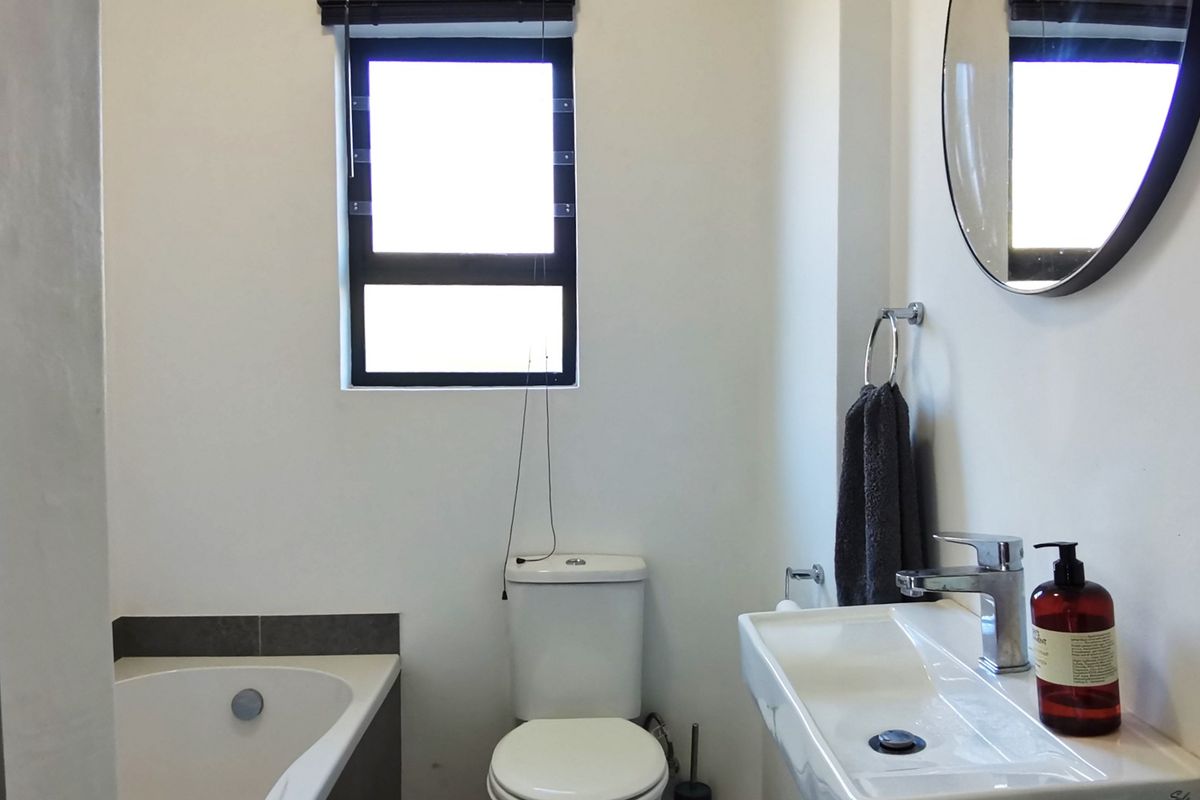A clean and functional bathroom featuring a built-in bathtub, a modern vanity basin with a mixer tap, and a standard toilet.