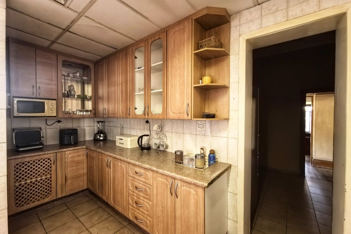 A functional kitchen featuring wood-look laminate cabinetry, tiled backsplash, and durable floor tiles, offering a classic layout with potential for modern updates.
