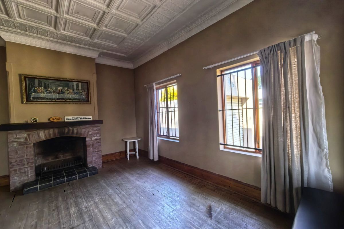 Spacious living room featuring a classic brick fireplace, original pressed metal ceilings, and timber flooring, offering a character-filled space ready for renovation.