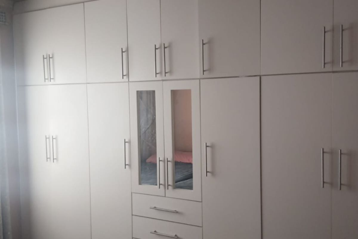 A bedroom featuring extensive floor-to-ceiling built-in white cabinetry with integrated drawers and mirrored panels.