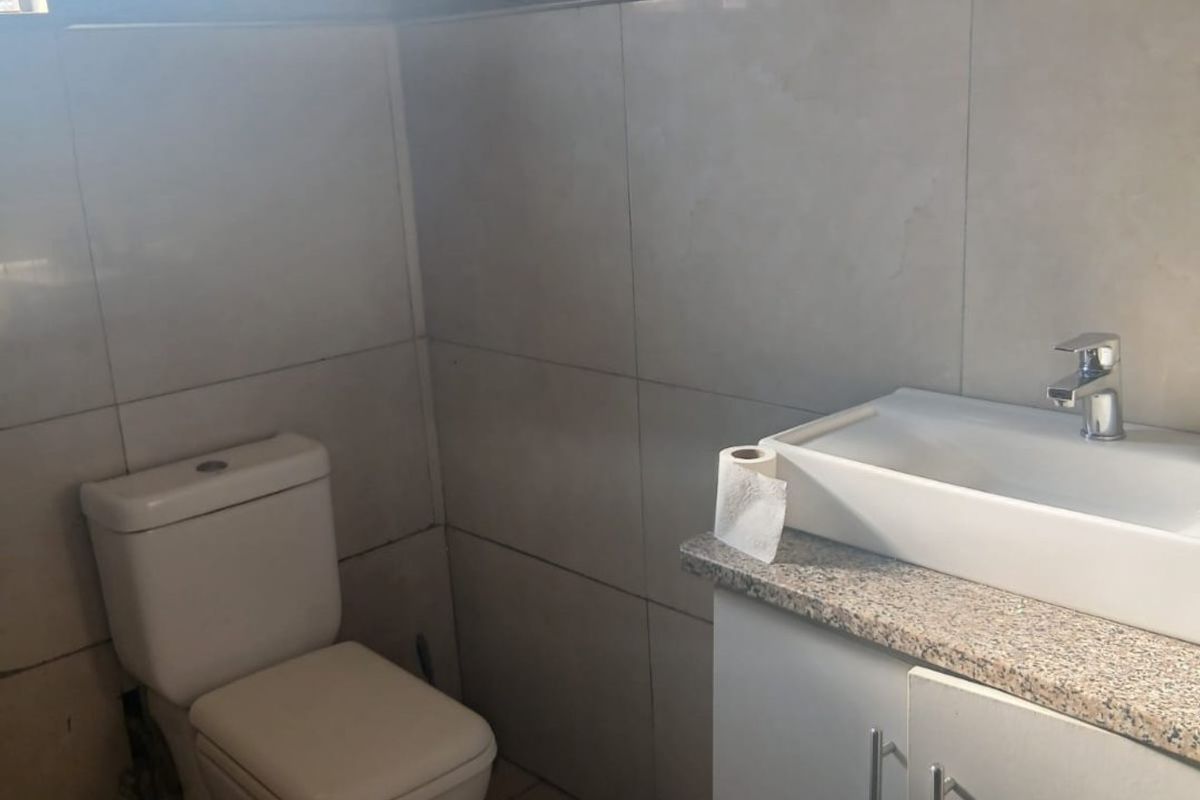 A functional bathroom featuring a vanity cabinet with a granite countertop, basin, and toilet, finished with neutral wall and floor tiles.