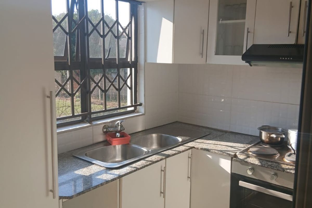 A compact, functional kitchen featuring white cabinetry, granite countertops, a double sink, and built-in oven with hob and extractor fan.