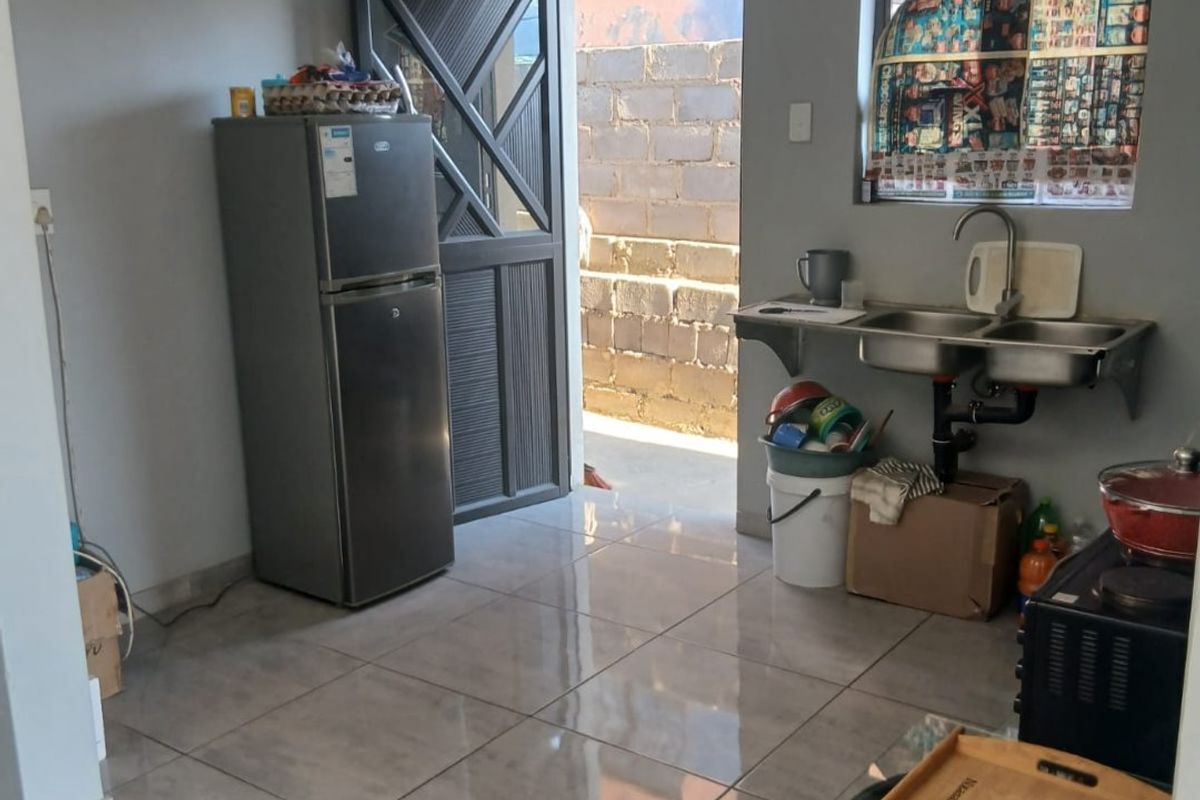 A functional kitchen area featuring tiled flooring, a stainless steel double sink, and direct access to an exterior courtyard through a security door.