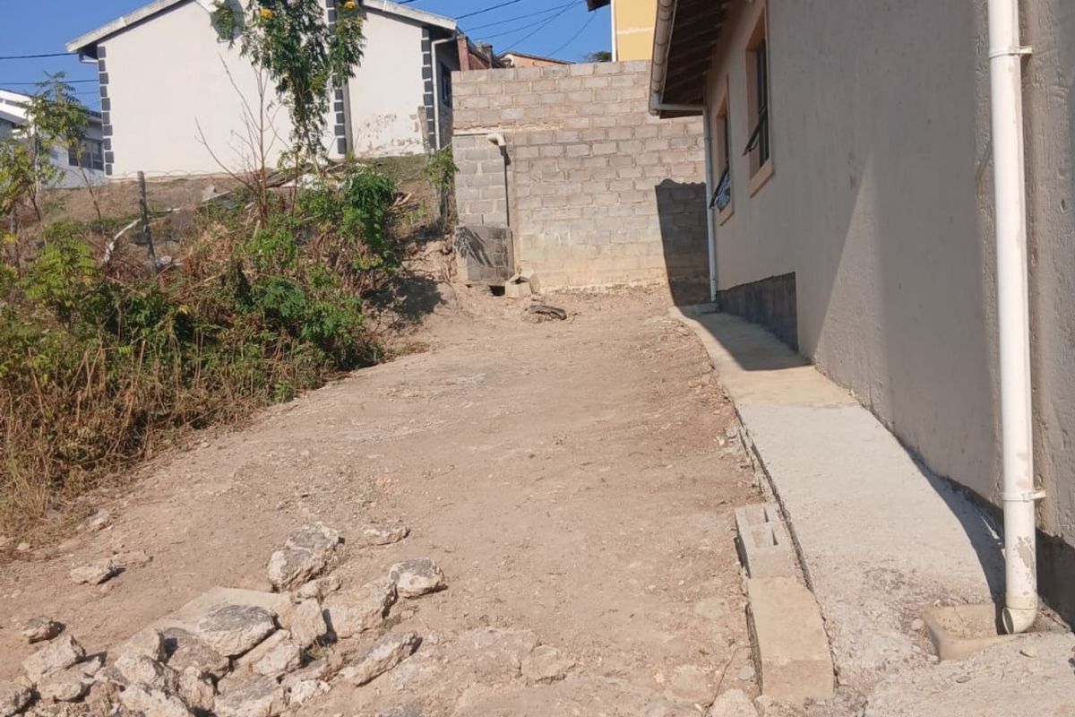 Rear exterior area showing unfinished ground, rubble, and concrete block boundary wall, requiring landscaping and surface improvements.
