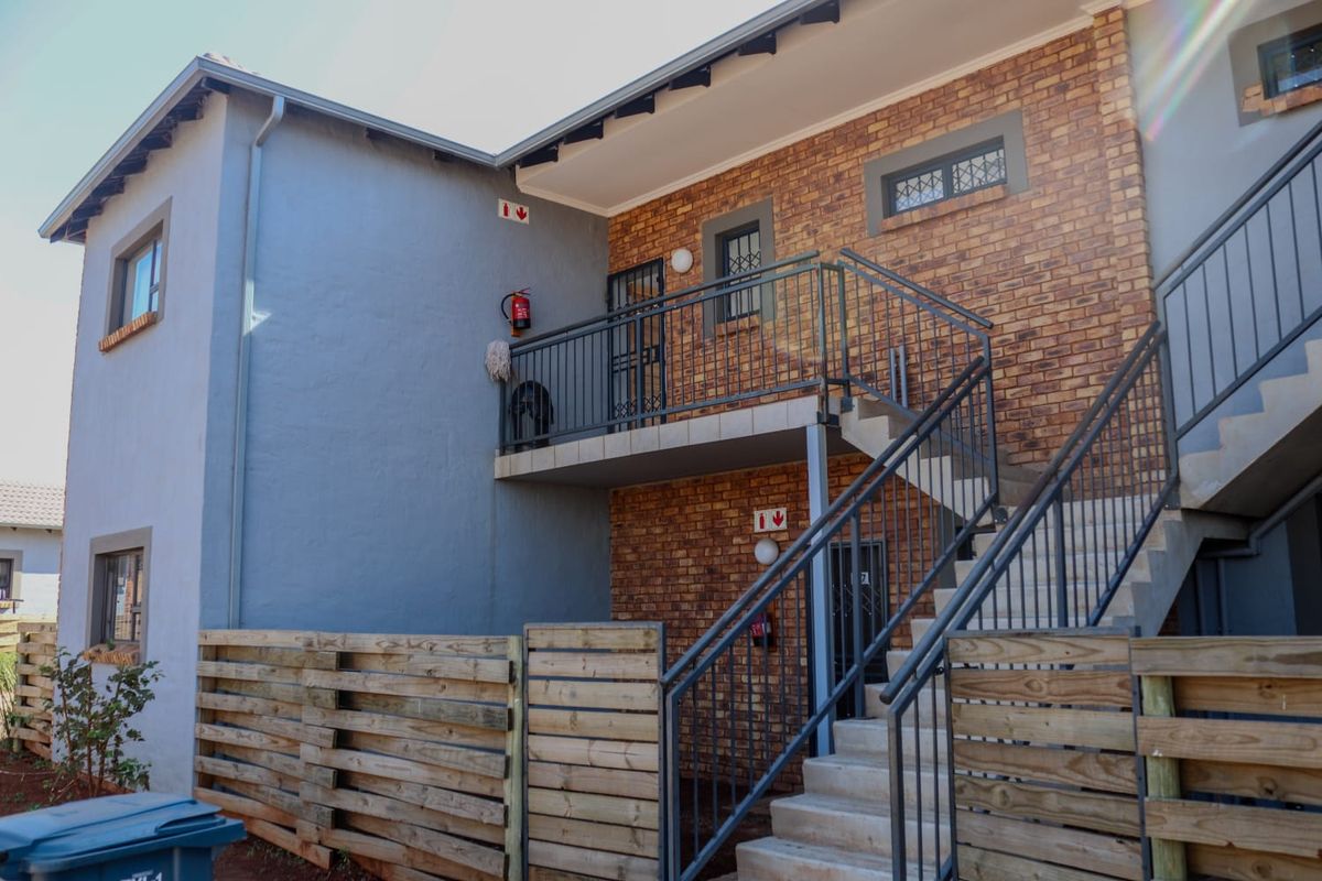 Exterior view of the apartment building featuring a brick facade, external staircase, and a private balcony with metal railings.