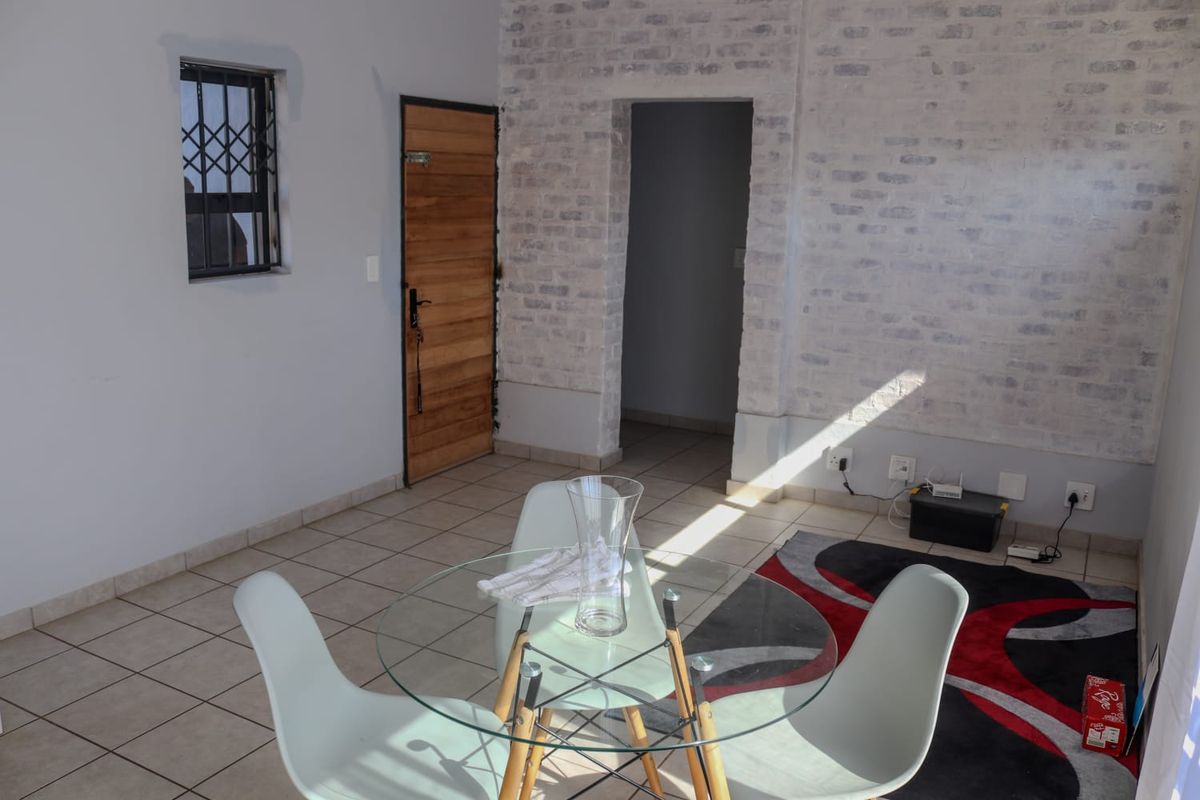 A living area featuring tiled flooring, an exposed white-painted brick feature wall, and a secure timber entrance door.