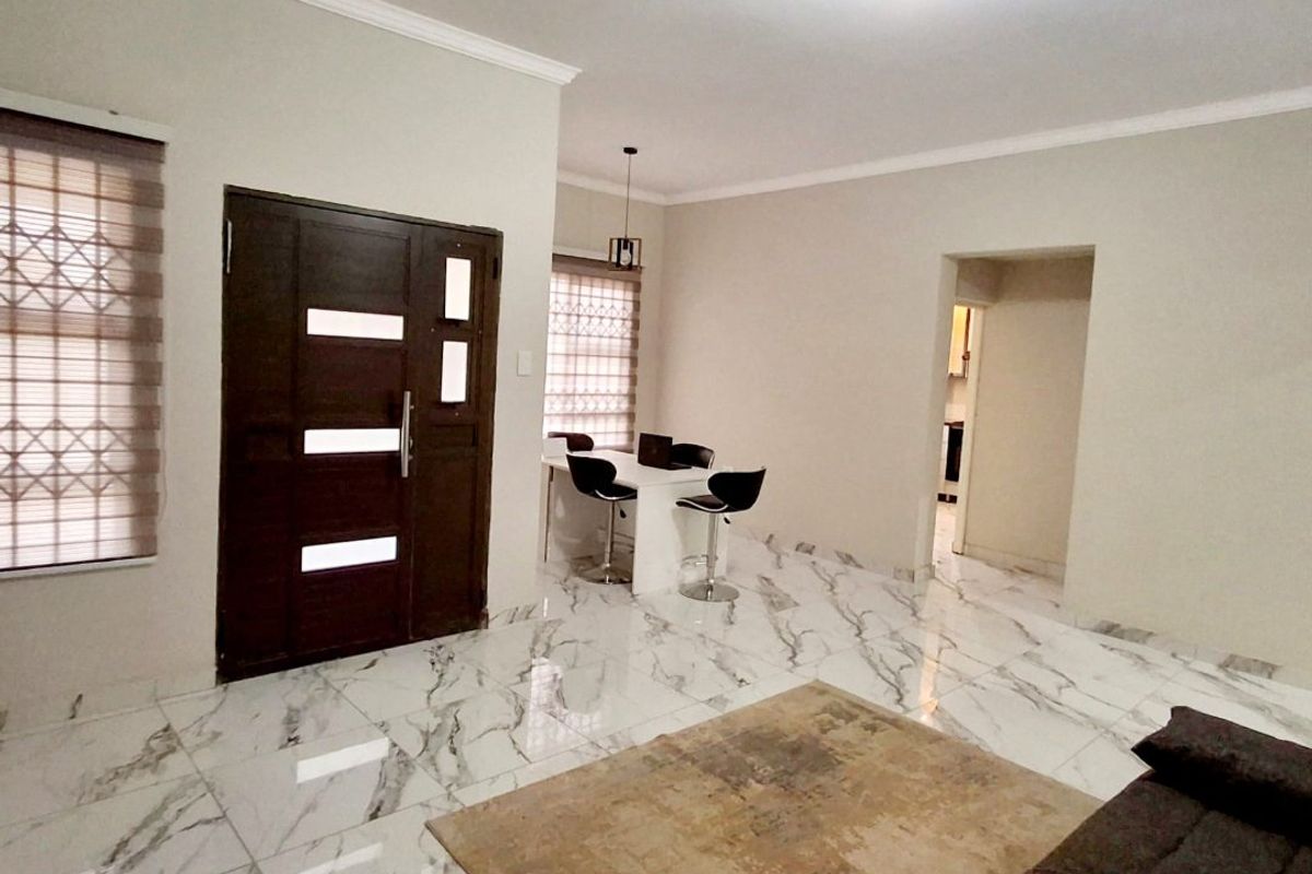 Open plan living area featuring polished marble-look floor tiles, neutral walls, and a modern dark wood entrance door with integrated glass panels.