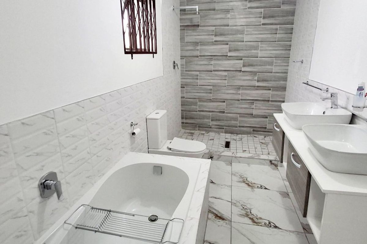 Modern bathroom featuring a double vanity with vessel sinks, a built-in bathtub, and a spacious walk-in shower with contemporary wall tiling.
