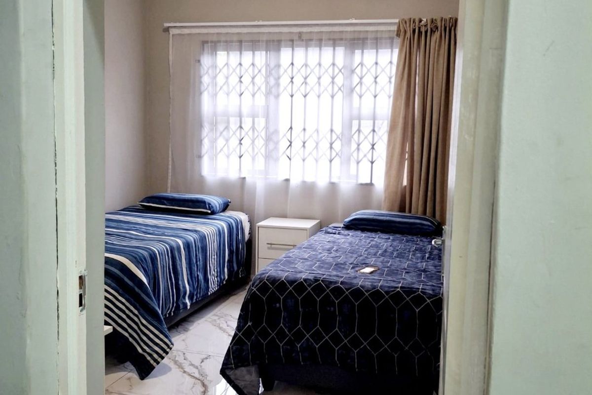 A bedroom featuring polished marble-look tiled flooring, neutral wall finishes, and a window fitted with a security gate and curtain rails.