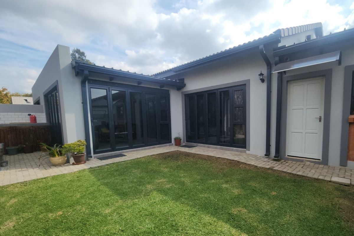 Rear view of the townhouse featuring a small lawn, paved pathways, and modern dark-framed bi-fold doors providing access to the interior living spaces.