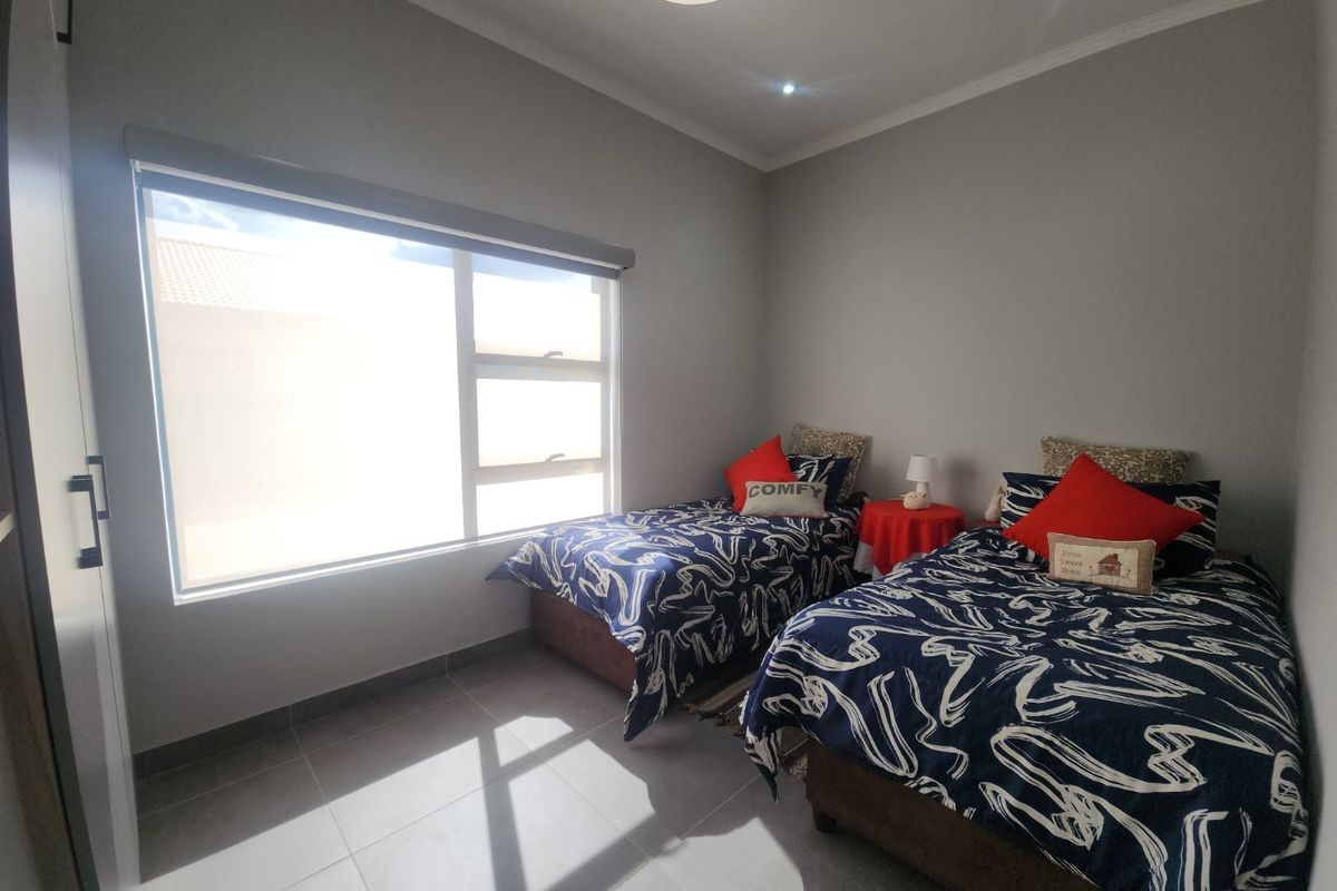A well-maintained bedroom featuring neutral tiled flooring, built-in cupboards, and a large window with a roller blind, providing ample natural light.