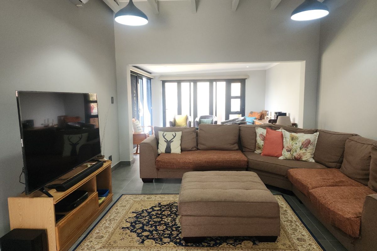 Spacious living room featuring exposed ceiling beams, tiled flooring, and large sliding glass doors that provide ample natural light and access to the outdoors.
