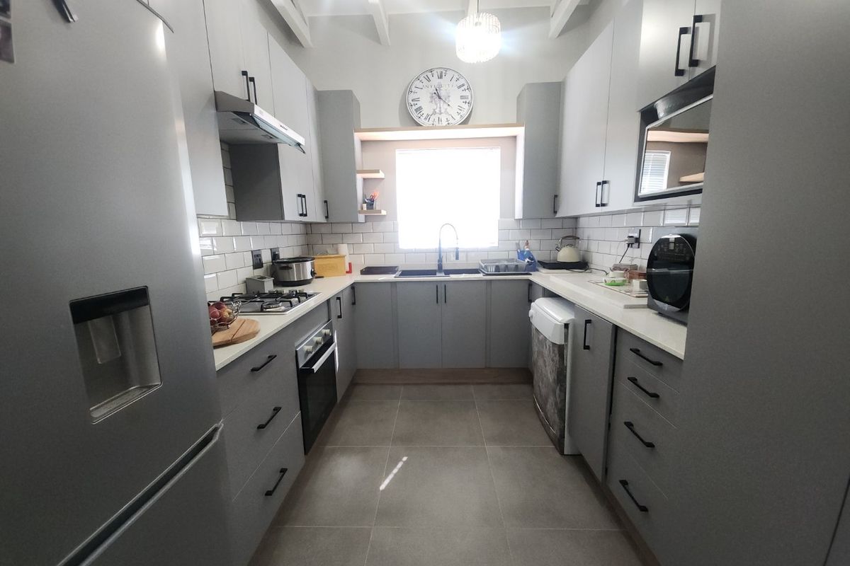 Modern galley-style kitchen featuring grey cabinetry, subway tile backsplash, gas hob, built-in oven, and tiled flooring with exposed ceiling beams.