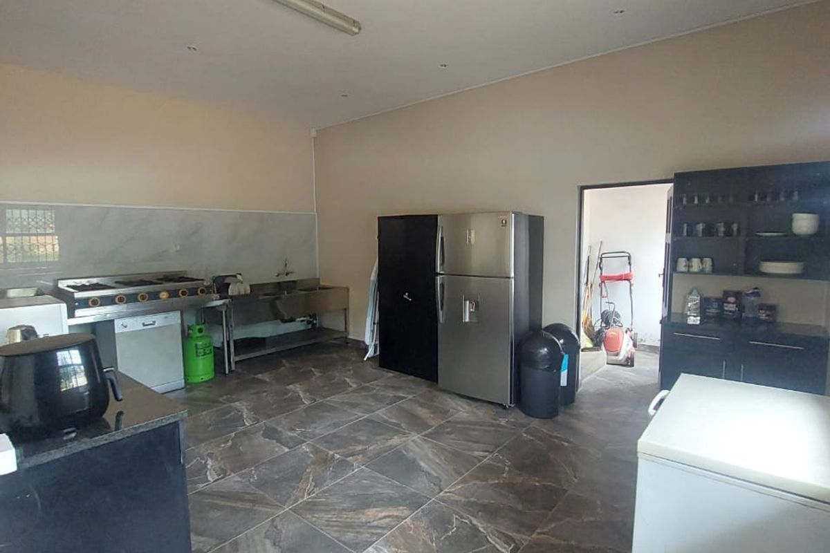 A functional commercial kitchen space featuring stainless steel appliances, tiled flooring, and built-in cabinetry with a marble-look splashback.