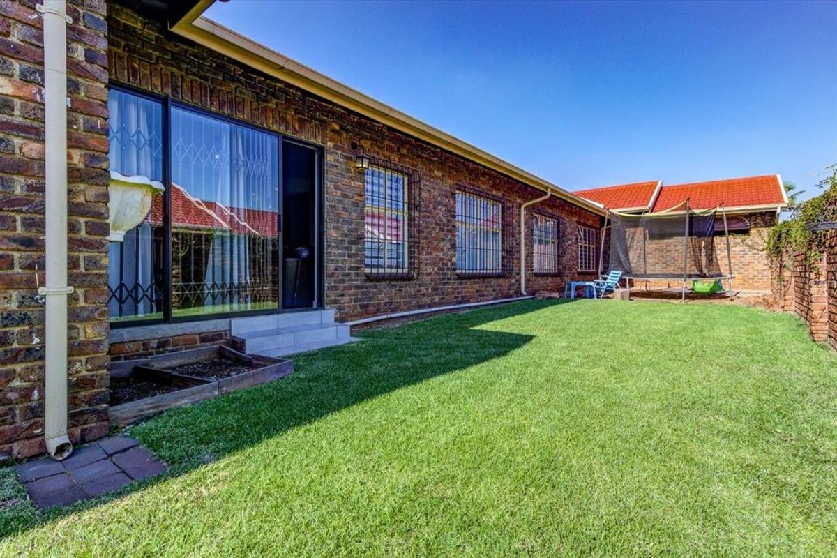 A rear exterior view of the townhouse featuring a face brick facade, sliding glass doors with security bars, and a well-maintained lawn area.