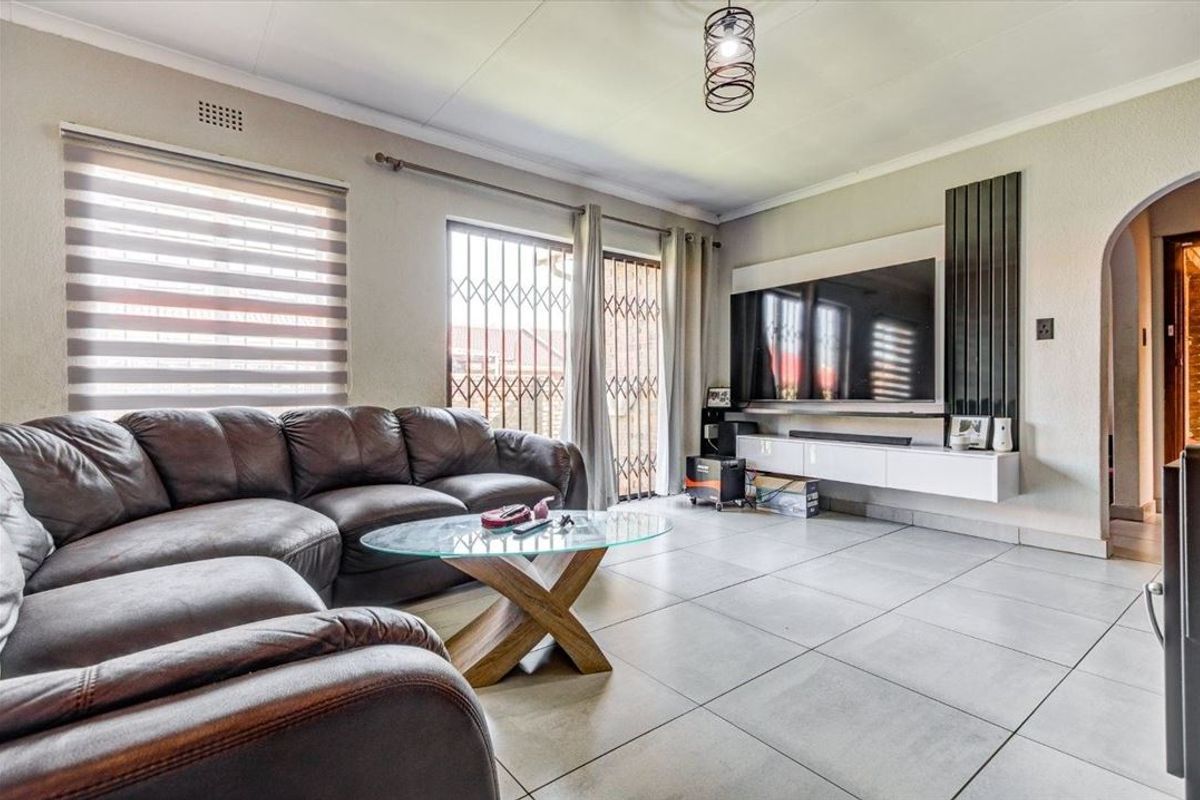A well-maintained living room featuring large format floor tiles, a wall-mounted media console, and sliding glass doors with security gates leading outdoors.