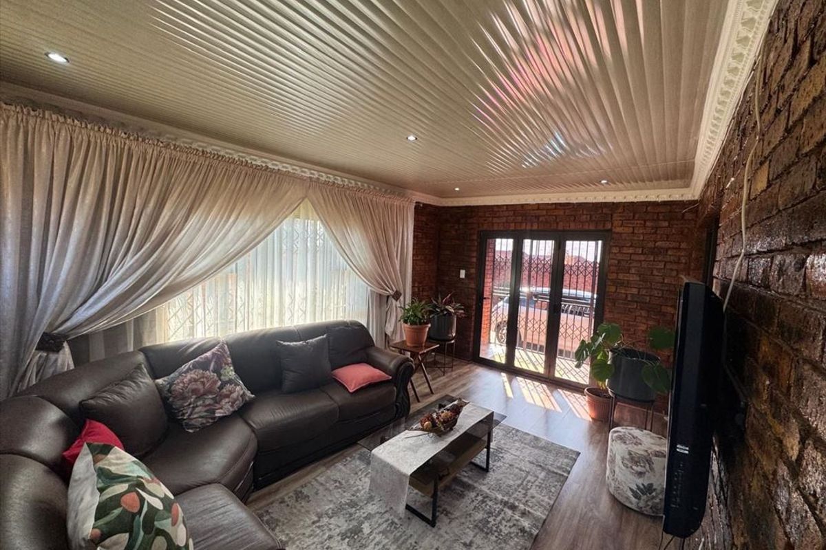 A cozy living room featuring exposed brick walls, laminate flooring, recessed lighting, and a sliding glass door with security gate access.