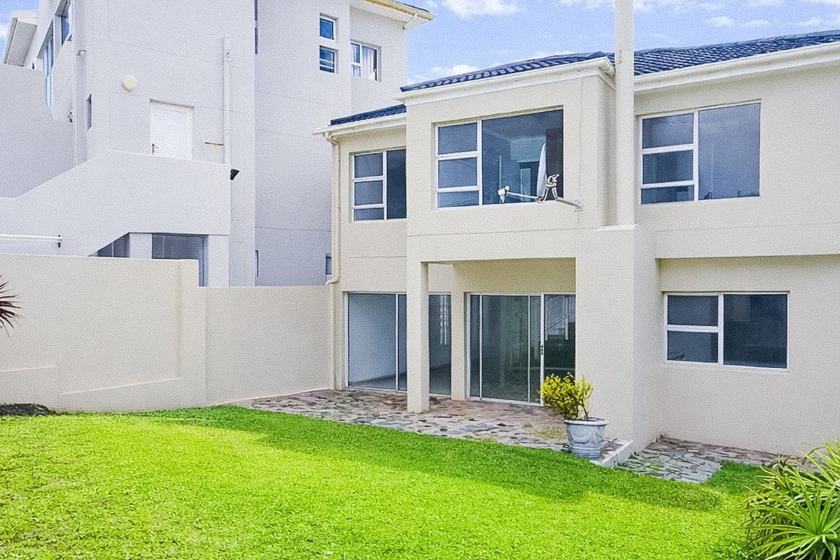 Rear view of a two-story townhouse featuring a paved patio area, sliding glass doors, and a private lawn with boundary wall.