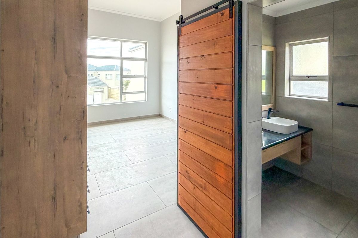 Spacious bedroom featuring neutral tiled flooring, a modern sliding barn door, and an en-suite bathroom with a contemporary vanity basin.