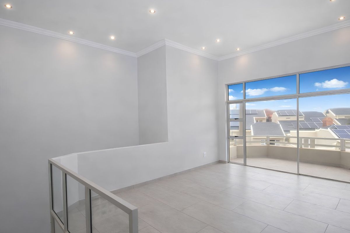 A bright, open-plan living area featuring neutral tiled floors, recessed lighting, and large sliding glass doors leading to a private balcony.