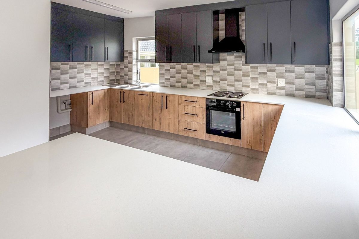 Modern kitchen featuring two-tone cabinetry, stone countertops, built-in oven, gas hob, extractor fan, and large sliding doors providing natural light.
