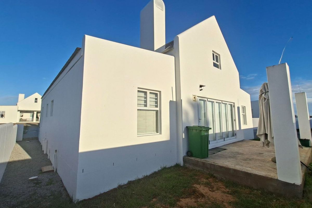Rear view of a white gabled house featuring a chimney, sliding glass doors, and a concrete patio area.