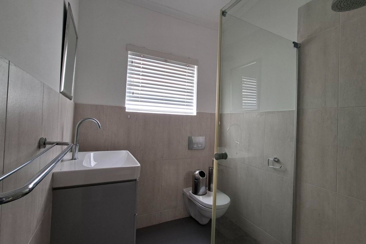Modern bathroom featuring a wall-hung vanity, wall-hung toilet with concealed cistern, and a glass-enclosed shower with neutral wall tiling.