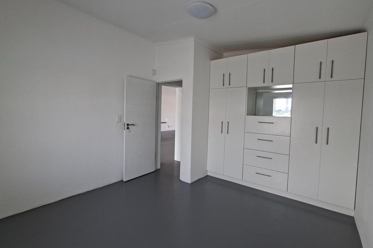 A clean, empty bedroom featuring neutral grey flooring, white walls, and extensive built-in cabinetry with integrated drawers and storage.