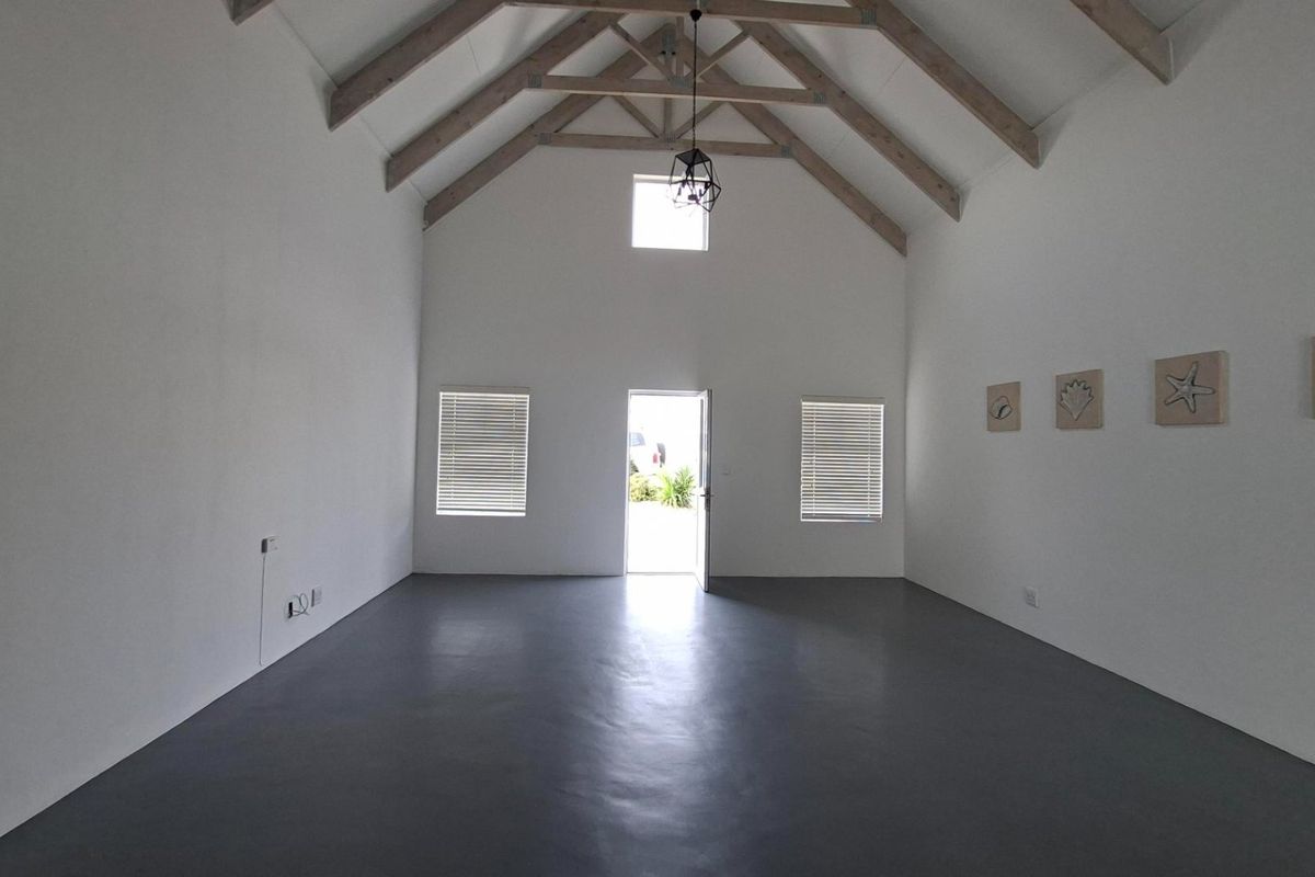 Spacious living area featuring high vaulted ceilings with exposed timber trusses, polished concrete floors, and abundant natural light.
