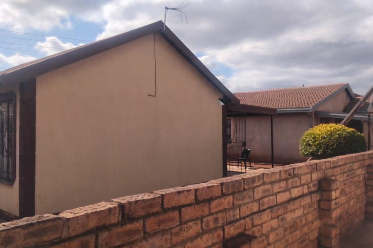 Rear view of the property featuring a brick boundary wall, tiled roof, and a small covered patio area.
