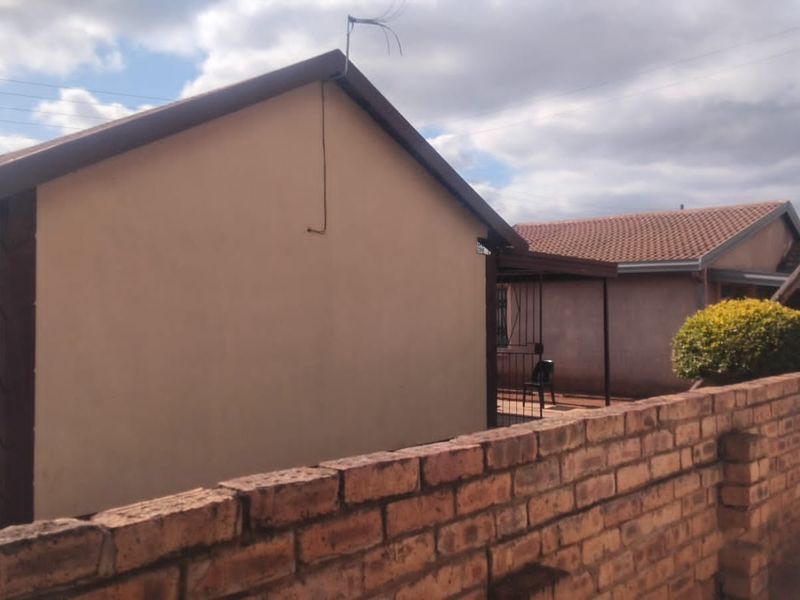 Rear view of the property featuring a brick boundary wall, tiled roof, and a small covered patio area.