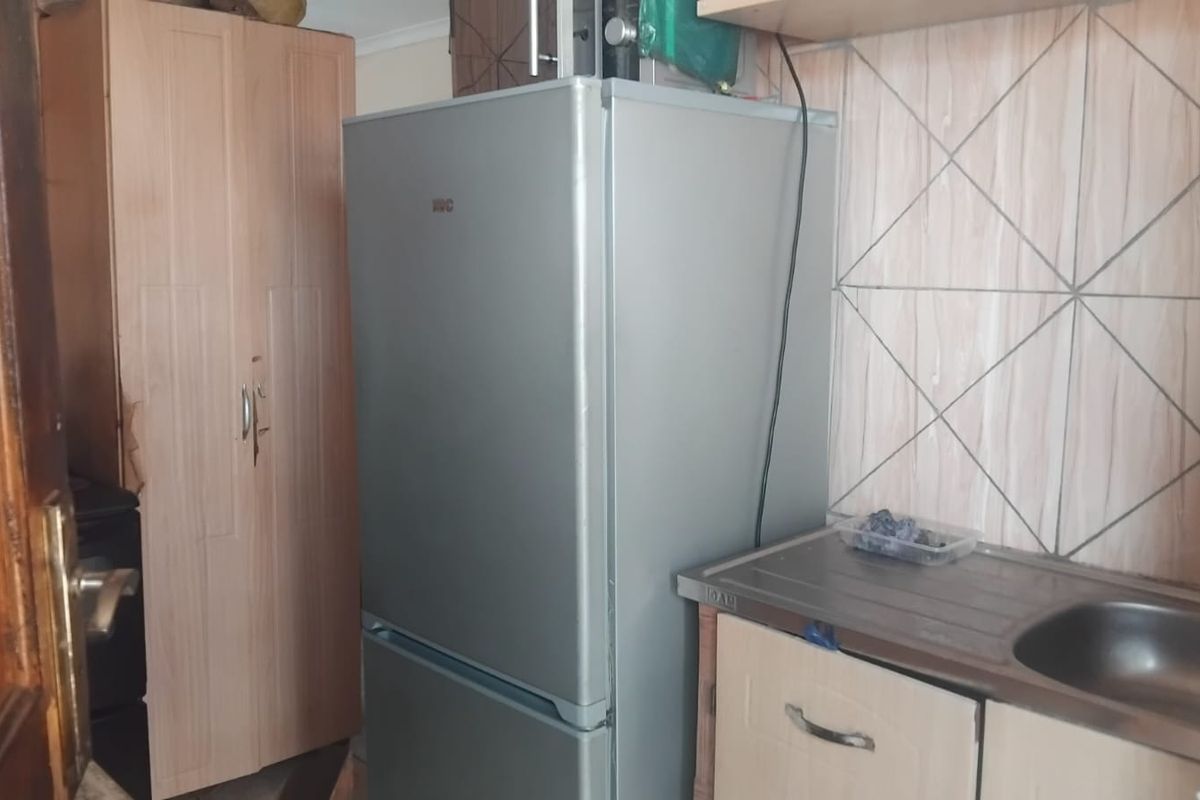 A compact kitchen area featuring a stainless steel sink, tiled splashback, and built-in cabinetry with visible signs of wear.