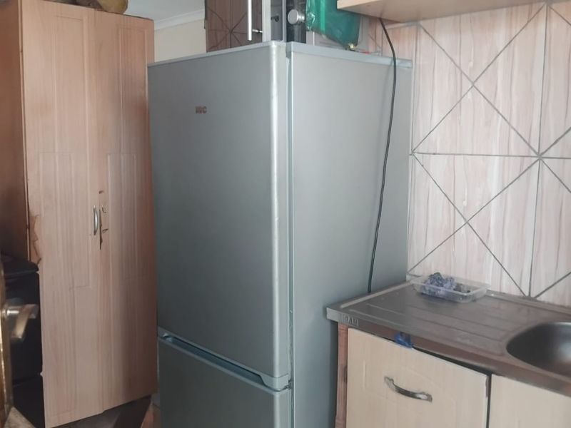 A compact kitchen area featuring a stainless steel sink, tiled splashback, and built-in cabinetry with visible signs of wear.