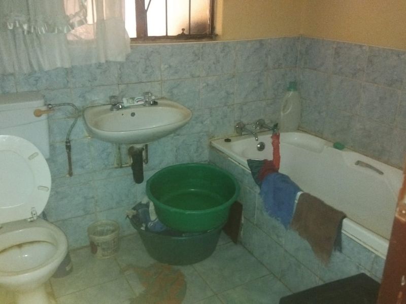 A dated bathroom featuring a standard bathtub, pedestal basin, and flush toilet with blue wall tiling and security bars on the window.