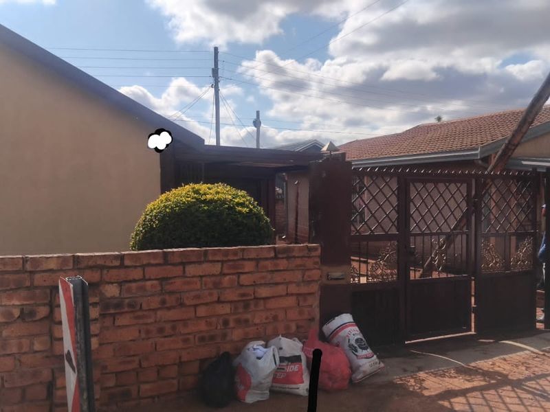 Front exterior view of a residential property featuring a brick boundary wall, metal security gate, and tiled roof structure.