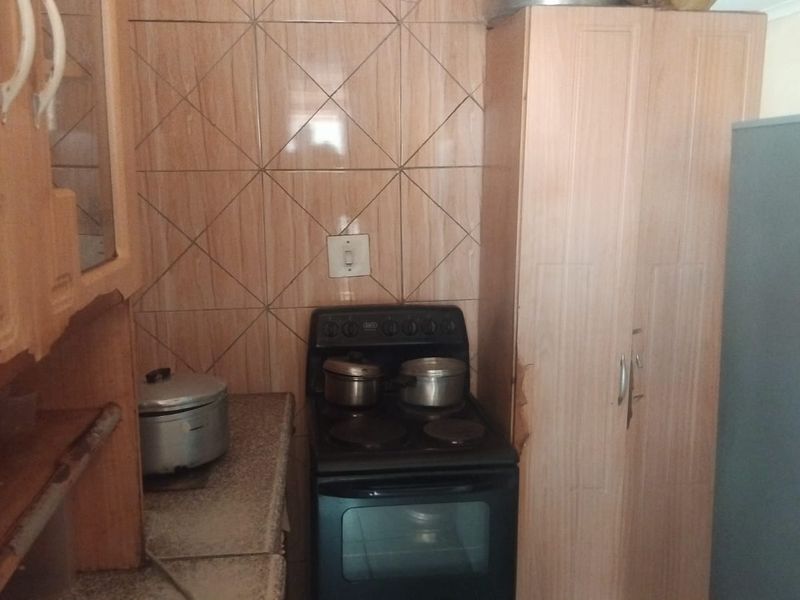 A compact kitchen featuring dated cabinetry, tiled backsplash, and a freestanding stove, showing signs of wear on the cabinet finishes.