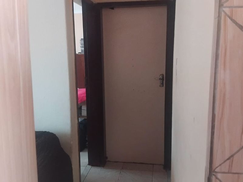A narrow interior hallway featuring tiled flooring and a standard internal door, showing signs of wear and tear.