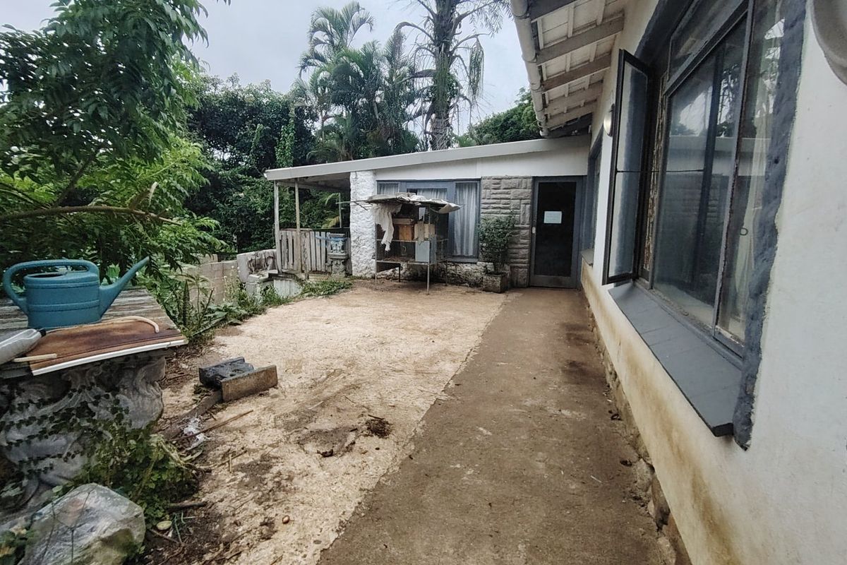 Rear exterior view of the property featuring a concrete pathway, covered patio area, and stone masonry detailing along the building facade.