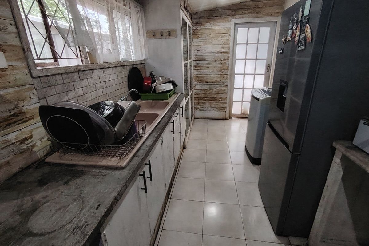 A functional kitchen area featuring tiled flooring, built-in cabinetry, and a double basin sink, requiring cosmetic updates to the wall finishes.