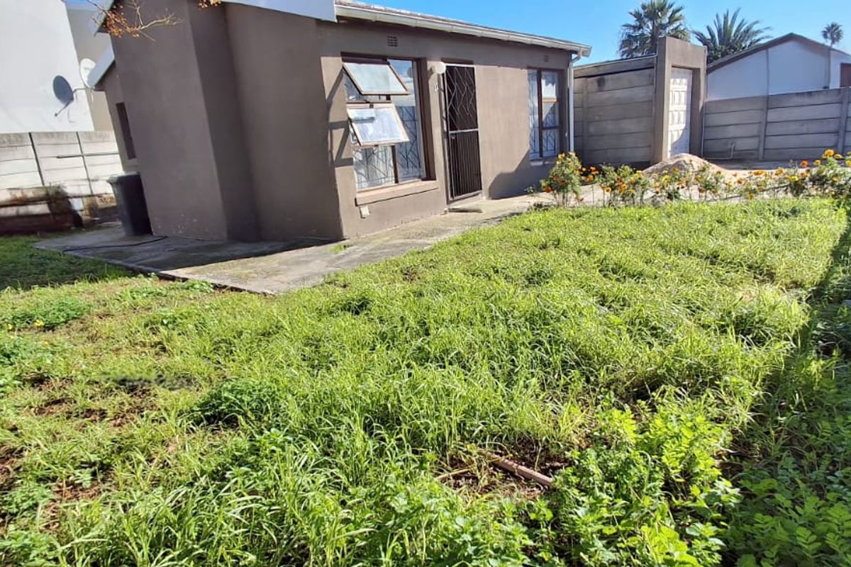 Rear view of the property featuring a private garden area, concrete boundary walls, and a small paved patio section.