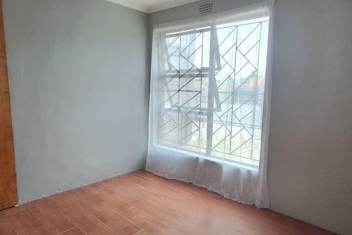 An empty bedroom featuring tiled flooring, a window with security bars, and a built-in cupboard.