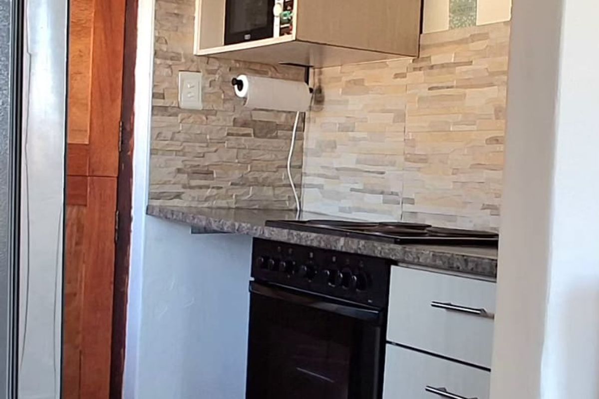 Compact kitchen featuring light-toned cabinetry, stone-look backsplash, built-in oven with hob, and integrated microwave space.