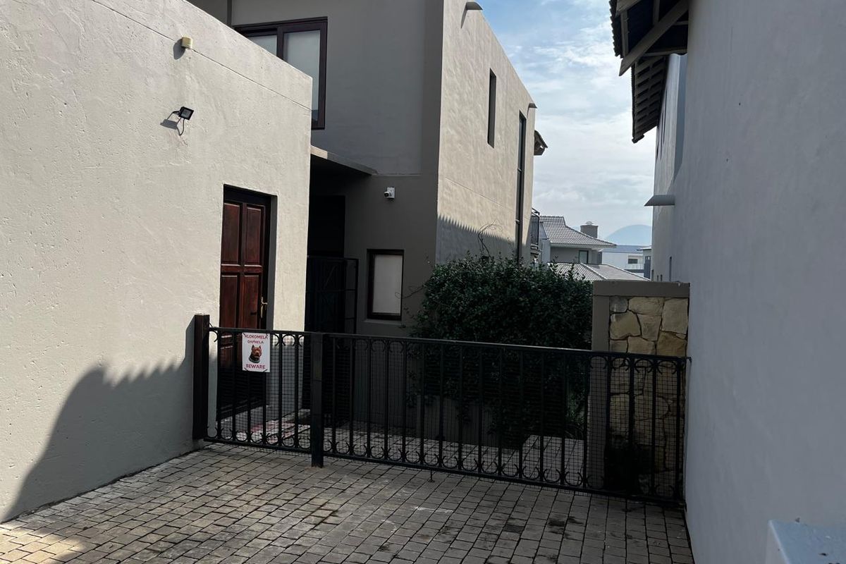 A paved side access area featuring a secure wrought iron gate, stone cladding detail, and a timber entrance door.