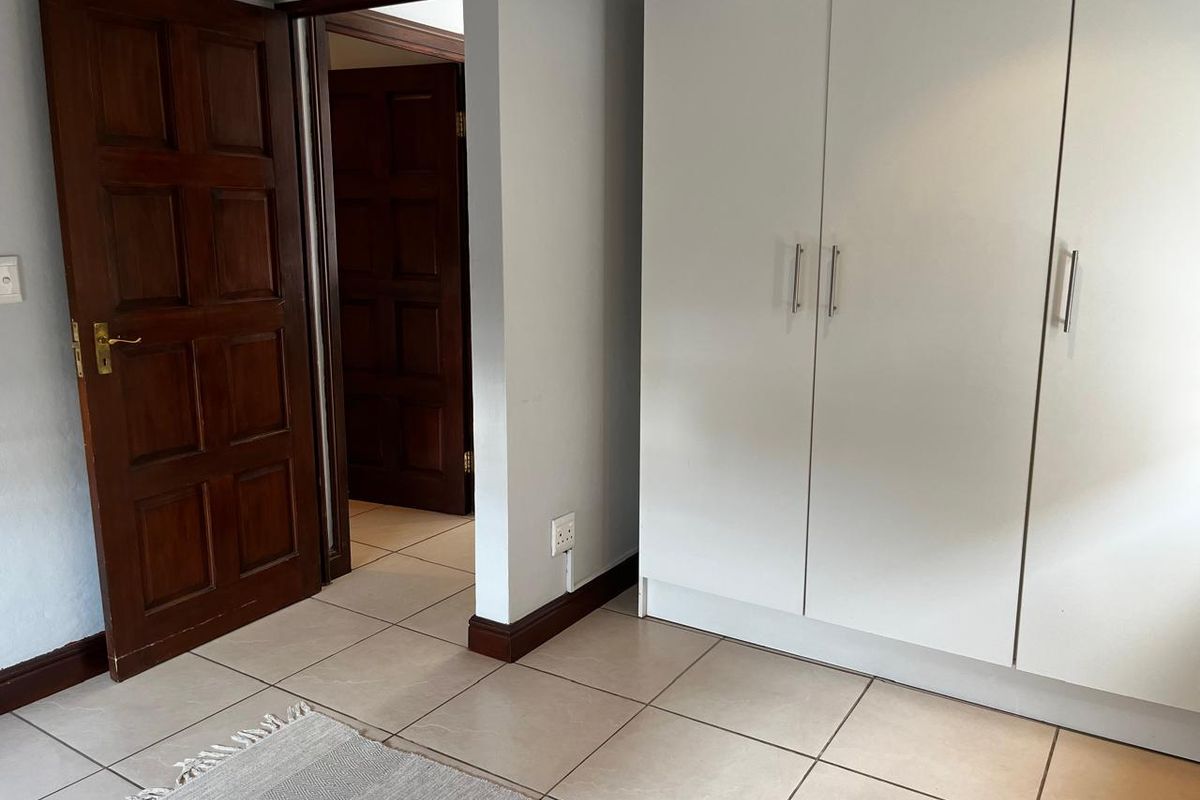 A clean bedroom interior featuring neutral tiled flooring, white built-in wardrobes, and traditional timber panel doors leading to an adjacent room.