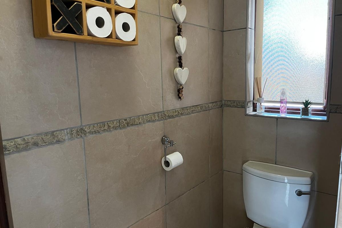 A compact bathroom featuring neutral ceramic wall tiles, a standard toilet, and a frosted glass window for privacy.