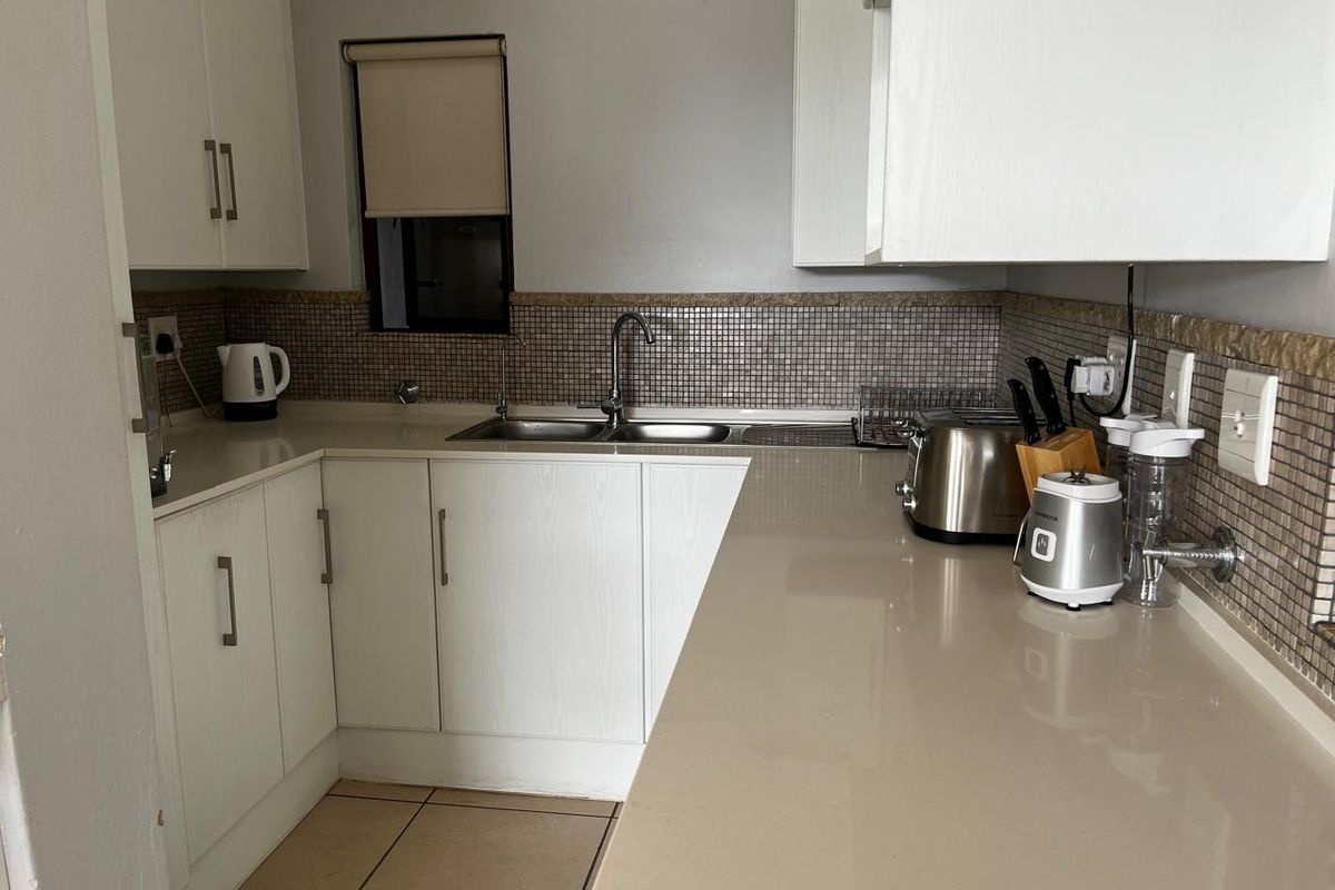 A functional kitchen featuring white cabinetry, stone countertops, and a mosaic tile backsplash with a double basin sink.