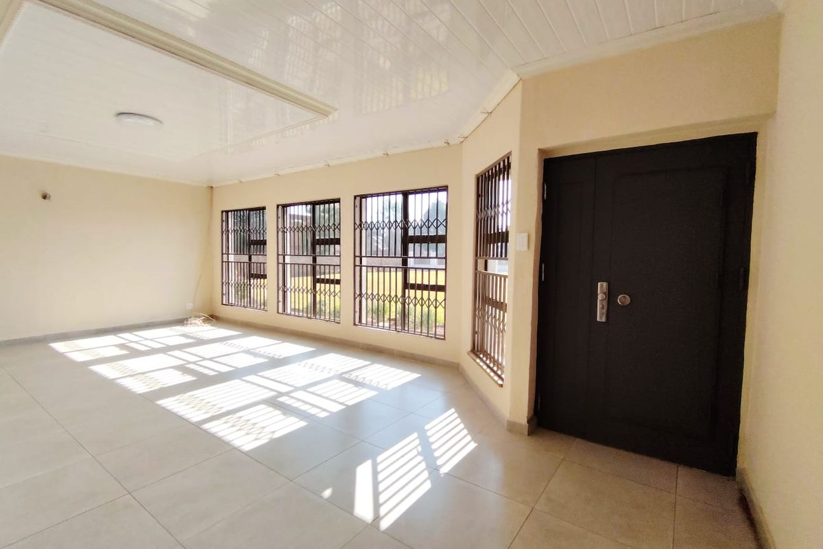 A bright, empty living area featuring large windows with security bars, tiled flooring, and a modern PVC ceiling.