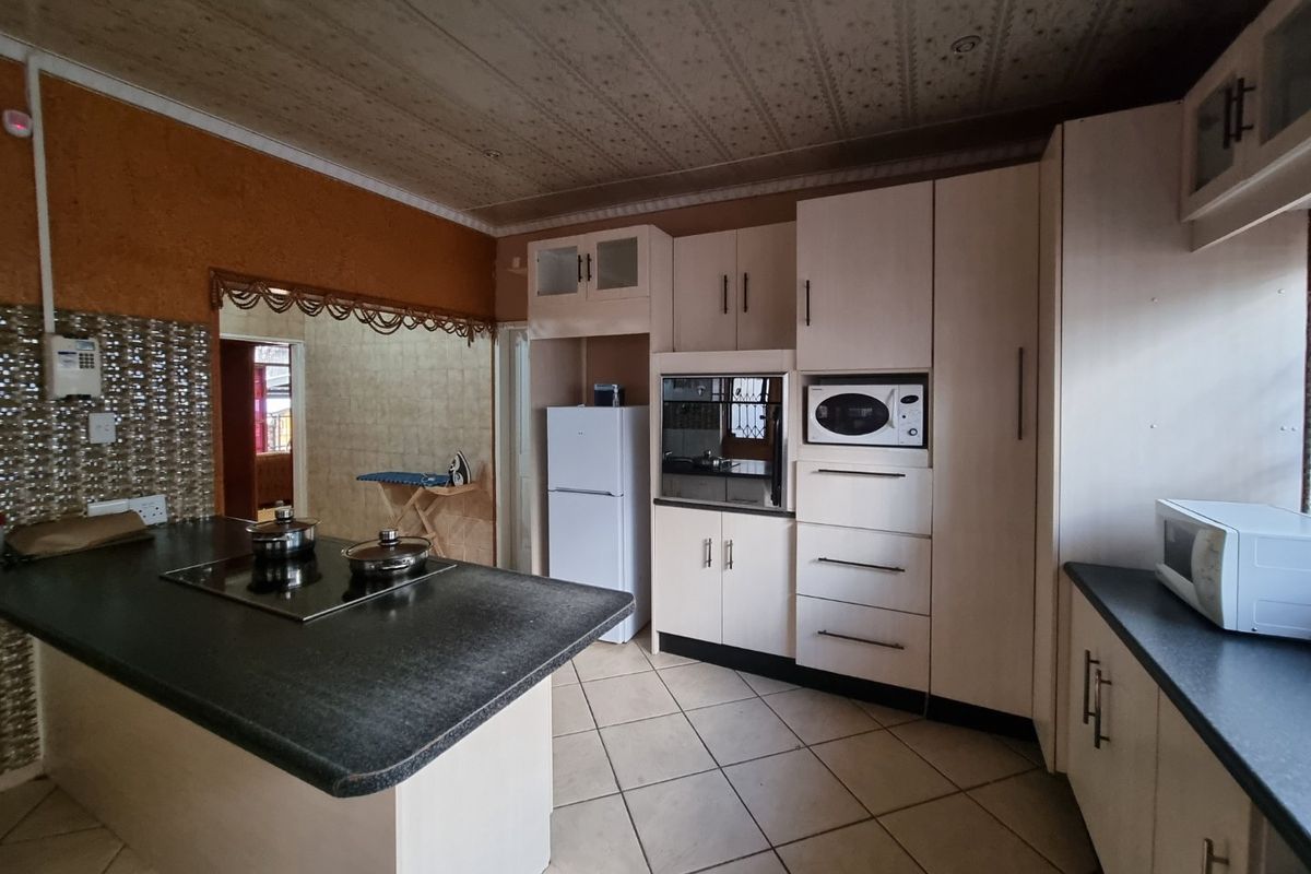 A functional kitchen featuring built-in cabinetry, a central island with a hob, and integrated appliances, offering a practical layout with potential for modern updates.