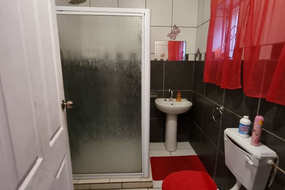 A functional bathroom featuring a shower enclosure, pedestal basin, and toilet with contrasting wall tiling.
