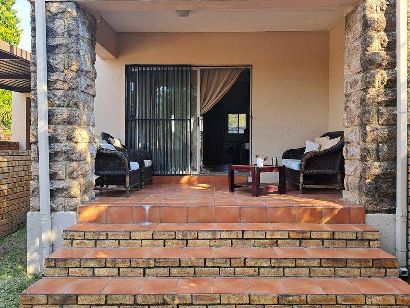 Covered patio area featuring stone-clad pillars and tiled steps leading to a sliding glass door entrance.